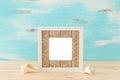 Blank white photo frame and sea shells over wooden table and pastel blue background. Ready for photography montage Royalty Free Stock Photo