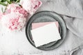 Blank white and pink paper postcard, on retro metallic tray, peony flowers and grey linen napkin on grunge stone background