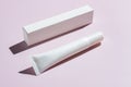 blank white plastick package for eye cream or face concentrate next to paper box on pink background with trendy harsh