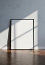 Blank white poster in black frame leaning against textured wall with window light Royalty Free Stock Photo