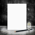 Blank White poster with lightbulb and pencil in a glossy concrete floor and black grunge cement wall