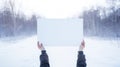 Blank white poster in woman hands in winter snowy forest. Mockup