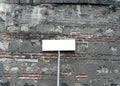 Blank white rectangular sign on weathered stone wall with rough texture and exposed bricks, perfect for mockup or Royalty Free Stock Photo