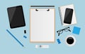 Blank white sheet on clipboard with pencil, smartphone, notebook, eyeglasses, coffee cup, digital tablet and post it paper on blue