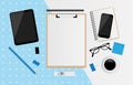 Blank white sheet on clipboard with tablet, coffee cup, notebook, donut, USB Flash Drive, eyeglasses and smartphone on blue and