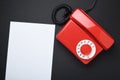 Blank white sheet next to a red vintage landline telephone on a black background. Place for text. Royalty Free Stock Photo