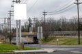 Blank white sign on long post near a street that goes under a train trestle.