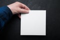 Blank white square sheet of paper in hand on a black background