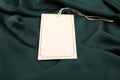 Blank white tag on green silky fabric, closeup. Space for text