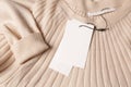 Blank white tags on beige sweater, top view. Space for text Royalty Free Stock Photo