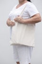 Close up of woman holding eco or reusable shopping bag against white wall background