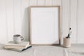 Blank wooden frame mockup with paint brushes, pencils in ceramic holder, cup of coffee and books on linen tablecloth