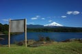 Blank wooden information board with view of snow capped Villarrica volcano and lake Villarrica.
