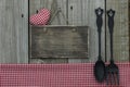 Blank wooden sign with red gingham heart and tablecloth and cast iron spoon and fork