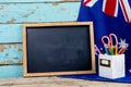 Blank writing slate by australian flag and desk organizer against blue wall with copy space