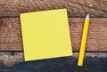 Blank yellow memo card and yellow pencil on a wooden table. A blank space to enter a note or insert graphics