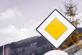 Blank yellow road sign meaning ` Yield pedestrians ` and `Main high  priority road` on sky background in nature, forest mountains. Royalty Free Stock Photo