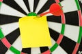 Blank sticky note on dartboard with dart