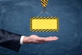 A blank yellow striped construction sign hanging from a crane hook above businessmen`s palm on chalkboard background.