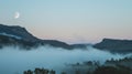 A blanket of mist settling over a tranquil valley as the moon rises higher in the sky. .