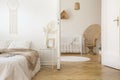 Blanket on white bed in bedroom interior with peacock chair next to child`s cradle