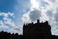 Dark silhouette scary looking medieval castle back-lit by sun behind passing clouds