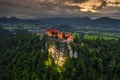 Bled, Slovenia - Aerial drone view of beautiful illuminated Bled Castle Blejski Grad with dark rain clouds, golden sunset