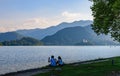 Evening View of Lake Bled from the city`s promenade. In the foreground are silhouettes of people with mobile phones