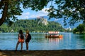 Two girls look at the landscape of Lake Bled, in the foreground are tree branches