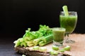 Blended Celery juice in welcome drink glass and bunch of fresh celery stalk on wooden table with leaves on black background. Food Royalty Free Stock Photo