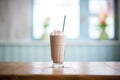 blended chocolate milkshake in tall glass with straw