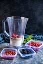 Blender with oatmeal, plastic plates, containers with raspberry, blackberry, red currant, cherry on a stone background