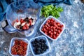 Blender with oatmeal, plastic plates, containers with raspberry, blackberry, red currant, cherry on a stone background