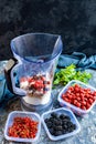 Blender with oatmeal, plastic plates, containers with raspberry, blackberry, red currant, cherry on a stone background