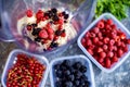 Blender with oatmeal, plastic plates, containers with raspberry, blackberry, red currant, cherry on a stone background