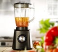 A blender on the table with some fruit and vegetables with blurred kitchen background.