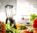 A blender on the table with some fruit and vegetables with blurred kitchen background.