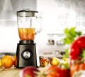 A blender on the table with some fruit and vegetables with blurred kitchen background.