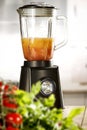 A blender on the table with some fruit and vegetables with blurred kitchen background.