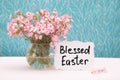 Blessed Easter - christian card with text and little pink flowers in vase on blue background