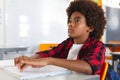 Blind african american schoolboy sitting at desk in classroom reading braille book with fingers