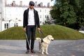 Blind man with cane and guide dog walking on pavement in town Royalty Free Stock Photo