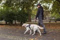 Blind man walking with a guide dog assistance through the autumn park Royalty Free Stock Photo