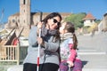 Blind mother with a white cane and her daughter talking sitting on a bench in the park and smiling. Visually impaired lifestyle