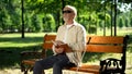 Blind pensioner reading braille book, sitting on bench in summer park, resting