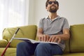 Blind smiling man sitting on sofa at home and reading tactile braille book. Royalty Free Stock Photo