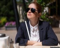 A blind woman in a business suit is sitting in an outdoor cafe.