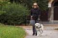 Blind woman in the company of a guide dog walking along a city park Royalty Free Stock Photo