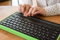 A blind woman uses a computer with a Braille display and a computer keyboard. Inclusive device.