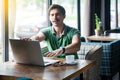 Blindness and way of business. Young blind businessman in green t-shirt sitting and trying to find his laptop with closed eyes